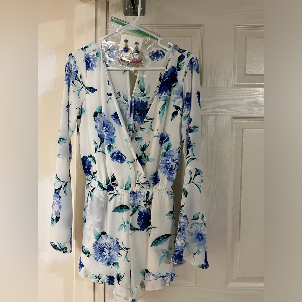 Floral long sleeve romper with ruffle edges. Elastic waistband. Crosses in front